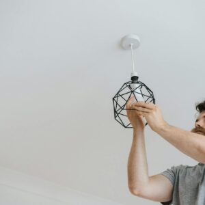 Photo by Anete Lusina A professional electrician skillfully installing a modern geometric ceiling lamp indoors.
