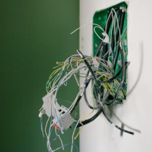 Opened power socket with various wires on white wall during repair at home