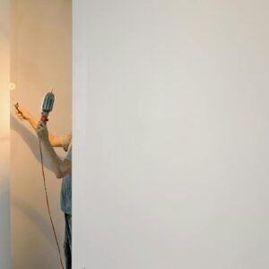 Unrecognizable person using a drill on a minimalist white wall in a home interior.